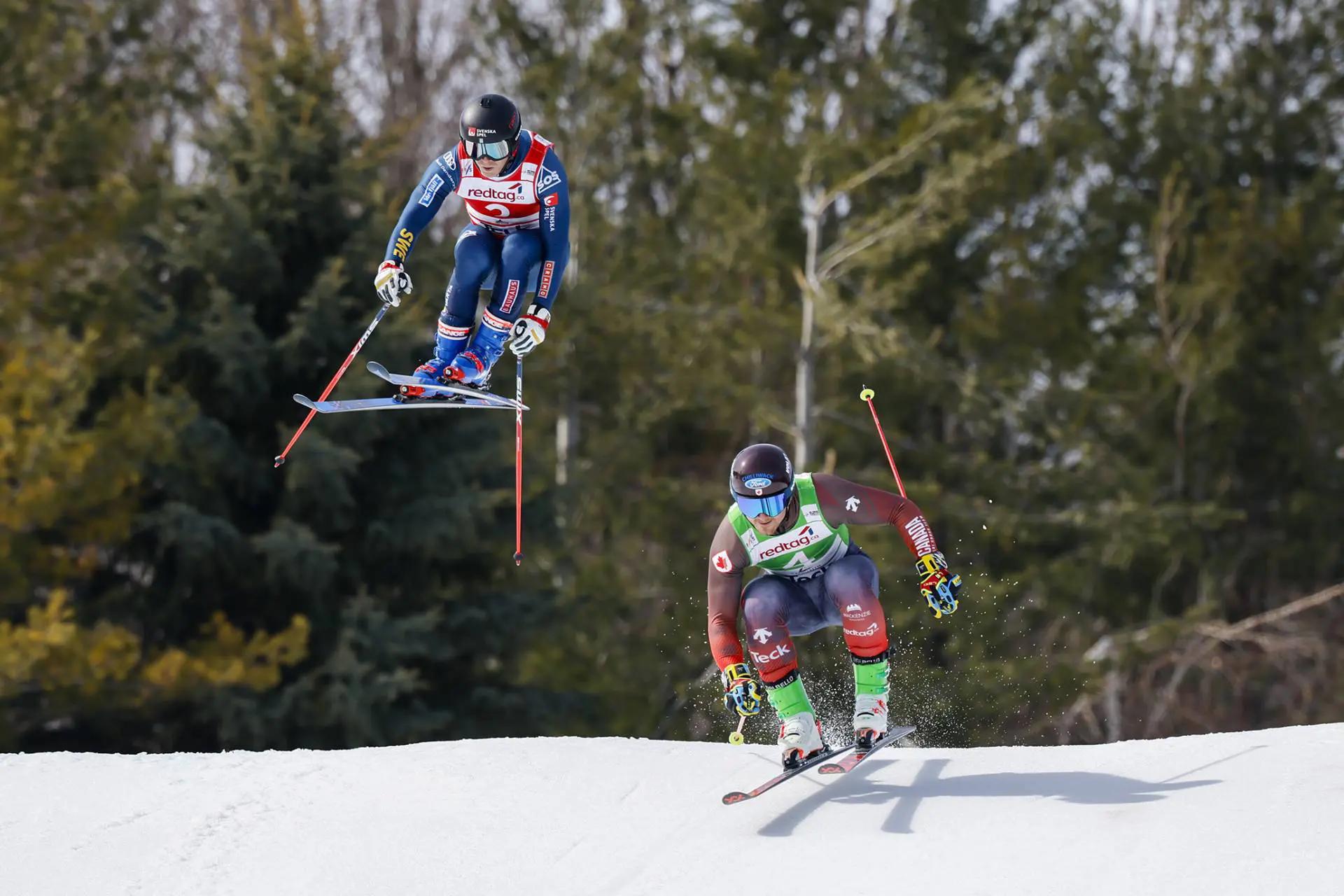 An action shot of 2 skiers launching over the snow