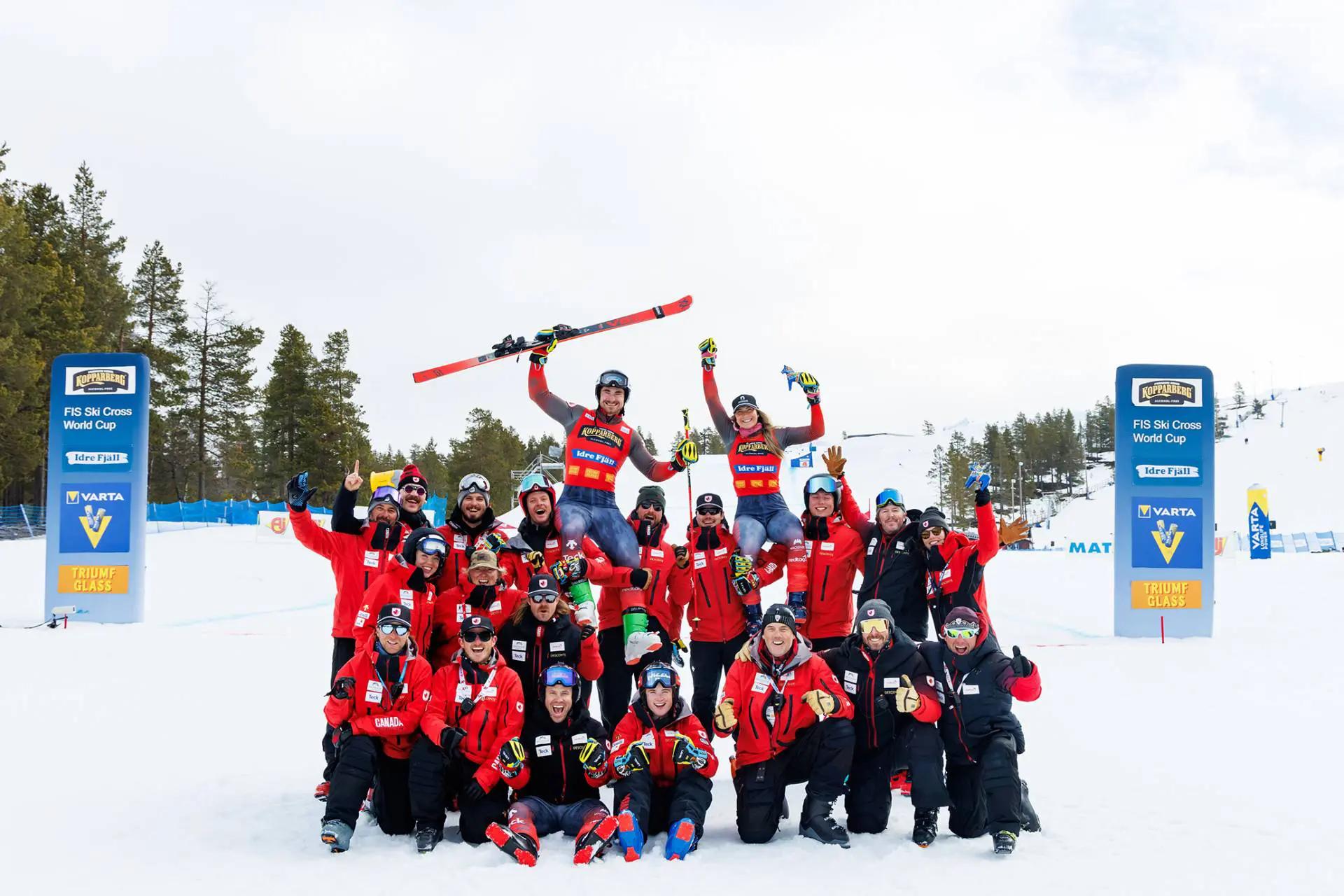 The team of skiers in red pose together in front of the slopes