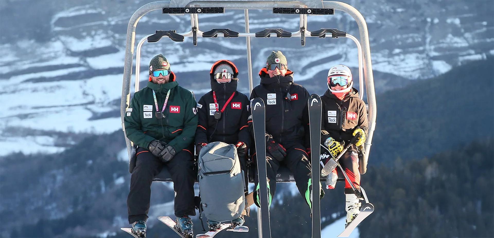 four people on a ski lift smiling at the camera with mountains in the background